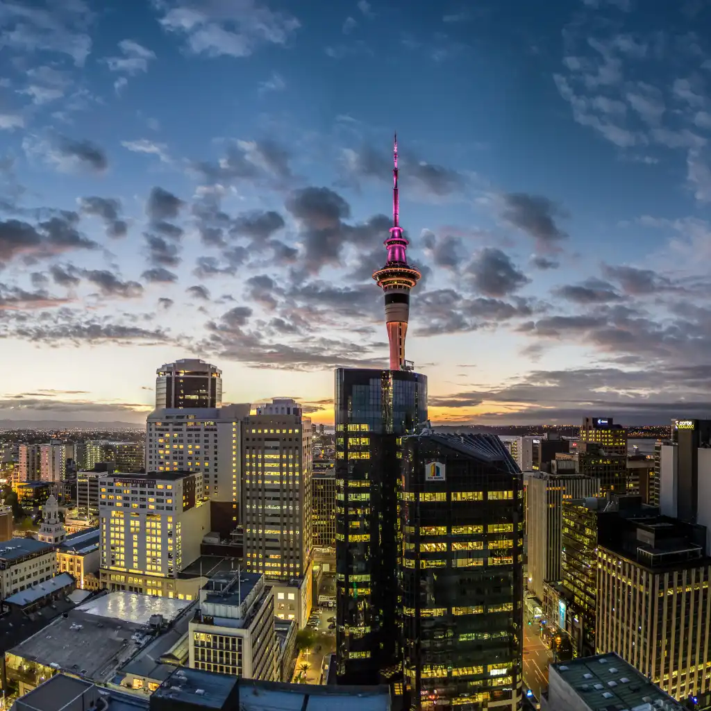 Auckland, New Zealand skyline at dusk with illuminated Sky Tower and glowing city buildings
