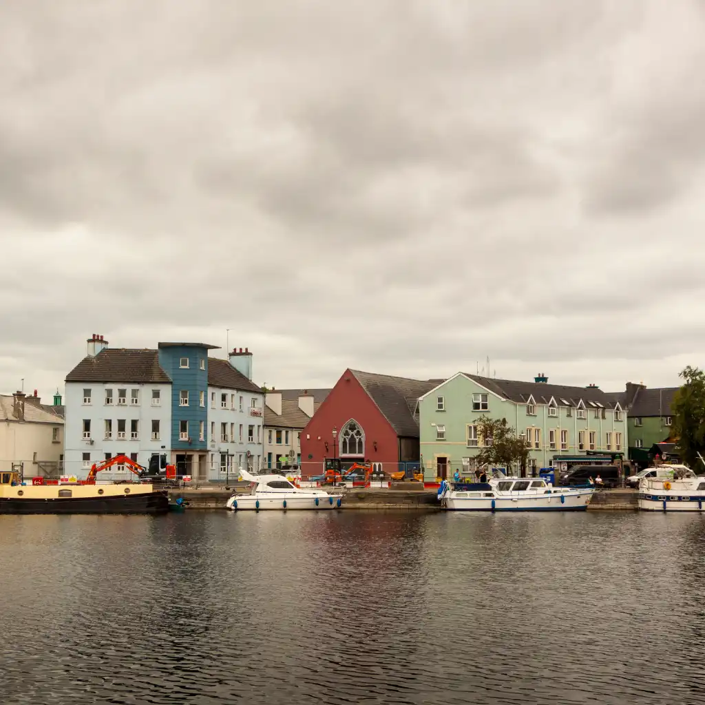 Colorful waterfront buildings and boats in an Irish coastal town under cloudy skies
